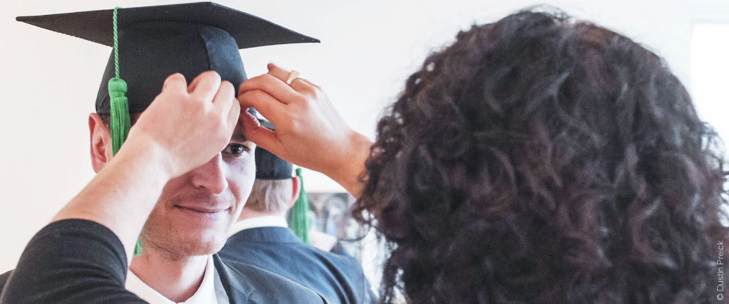 We see a dark-haired, curly-haired woman from behind straightening the doctoral hat of a doctoral student during a graduation ceremony at the WiSo faculty
